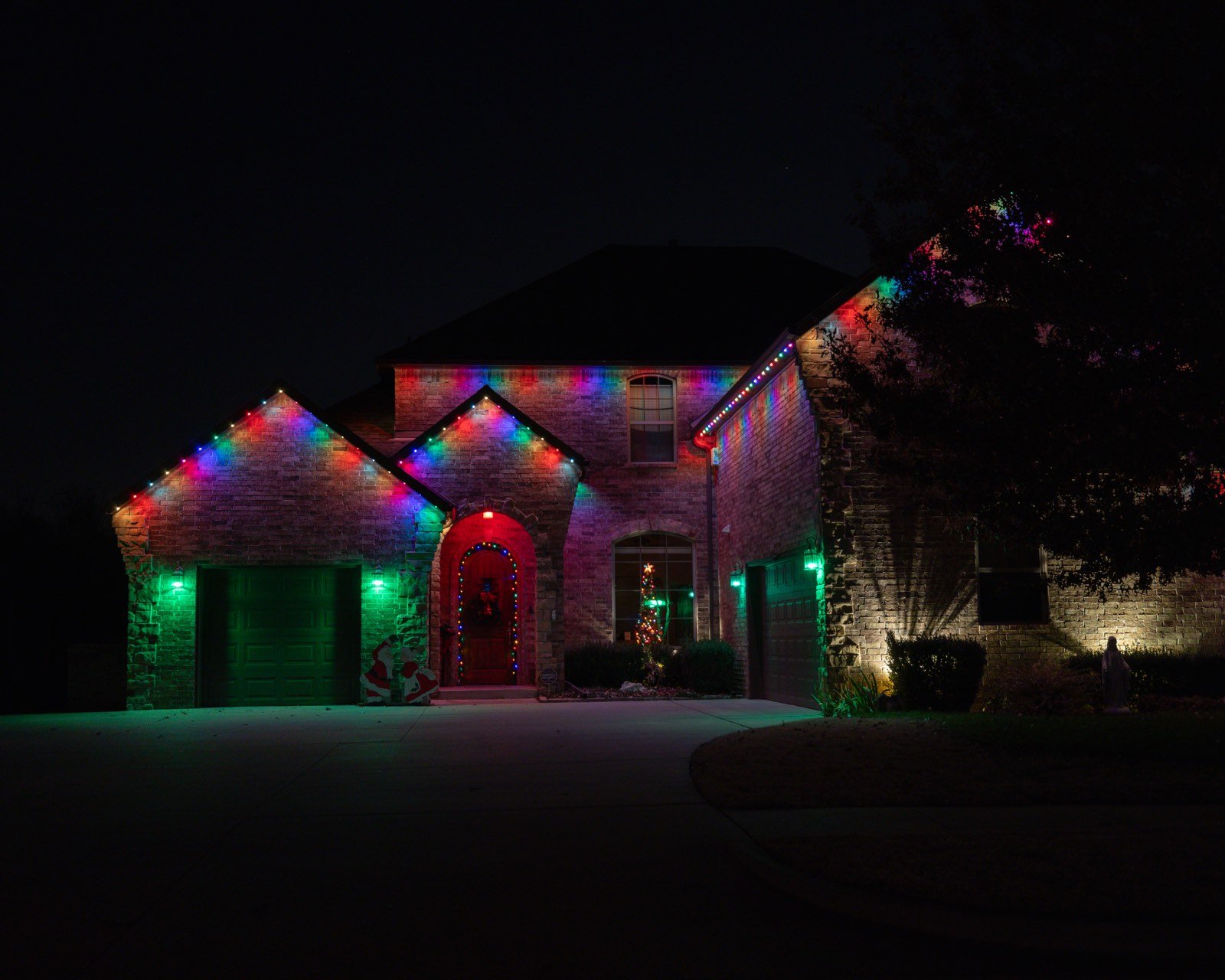 Stone home decorated with multicolor Christmas lights along the roofline and an inflatable Santa in the yard