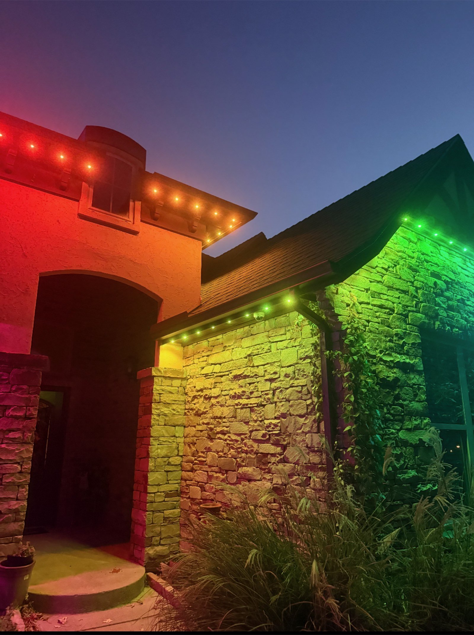 Stone home lit in team colors with zoned permanent roofline lighting